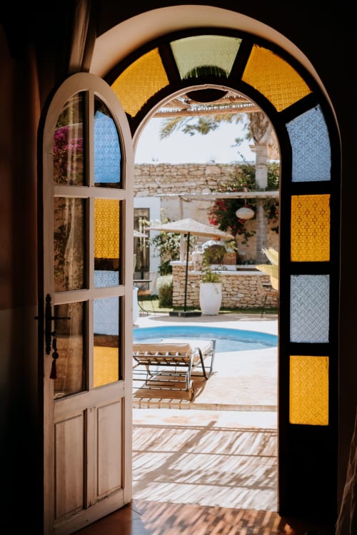 Portail en arc avec vitrail coloré ouvrant sur une cour piscine de l'hôtel Eucalyptus Ethnic à Essaouira, Maroc