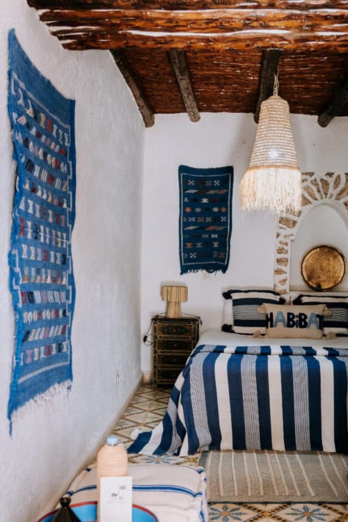 Acogedora habitación bereber en el hotel Eucalyptus Ethnic en Essaouira con ropa de cama rayada, vigas de madera y azul tradicional