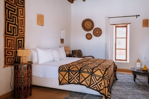 Habitación Ethnic Deluxe en el Hotel Eucalyptus de Essaouira con ropa de cama de patrones geométricos, arte textil en la pared y detalles de madera
