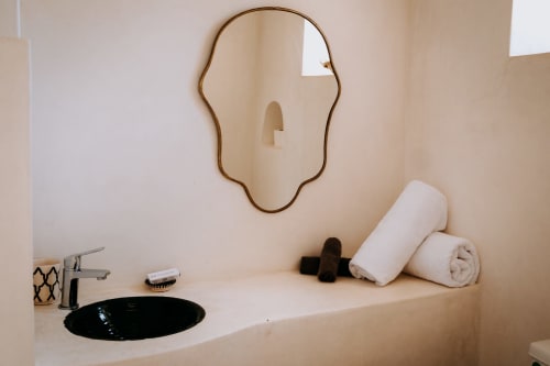 Modern bathroom vanity at Eucalyptus Ethnic hotel with black sink, brass mirror, and white rolled towels in Essaouira