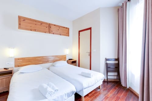 Chambre studio lumineuse à la Résidence Molière Montrouge avec lits jumeaux, tête de lit en bois et équipements modernes