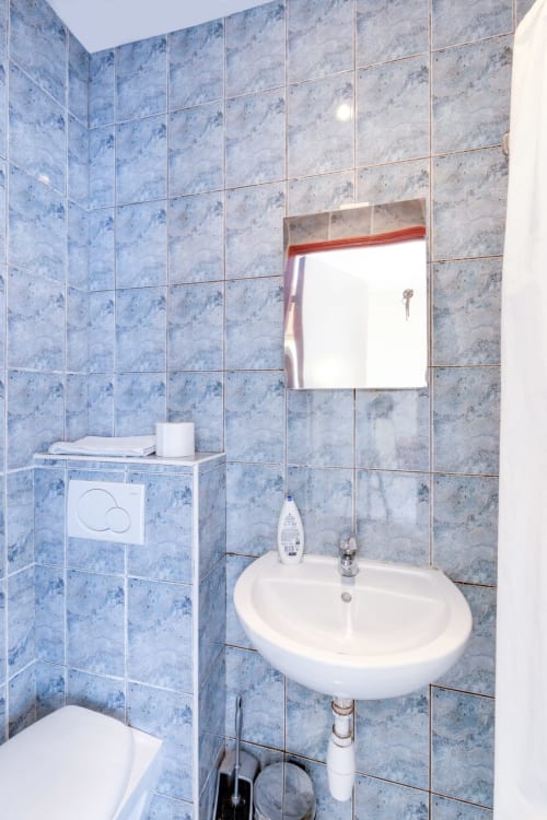 Salle de bain du studio à la Résidence Molière Montrouge avec carrelage bleu, lavabo, miroir, toilettes et articles de toilette