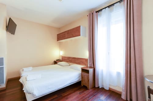 Chambre studio lumineuse à la Résidence Molière Montrouge avec lit double, mobilier en bois, télévision et rideaux roses