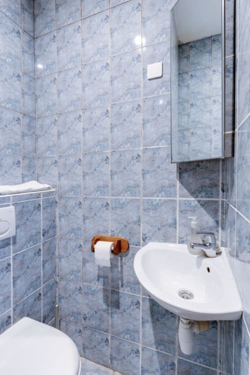 Salle de bain moderne aux murs en carrelage bleu, lavabo blanc d'angle, toilettes et porte-serviettes en bois à la Résidence Molière