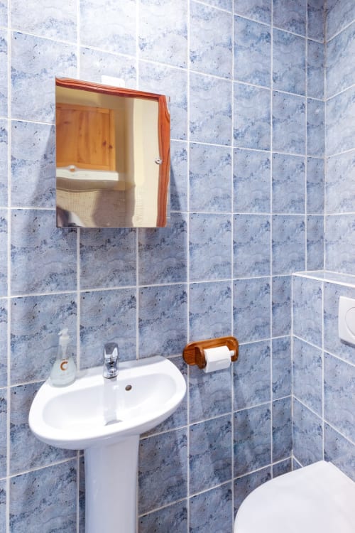 Salle de bains moderne avec lavabo sur colonne blanc, miroir encadré bois et murs carrelés bleus à l'hôtel Résidence Molière à Montrouge,