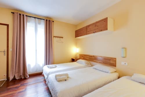 Chambre lumineuse à la Résidence Molière Montrouge avec trois lits, têtes de lit en bois, murs jaunes et accès à la terrasse