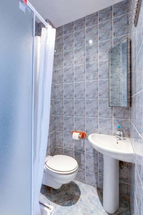 Salle de bain compacte de la résidence Molière avec toilettes blanches, lavabo sur colonne et carrelage gris dans l'hôtel de Montrouge
