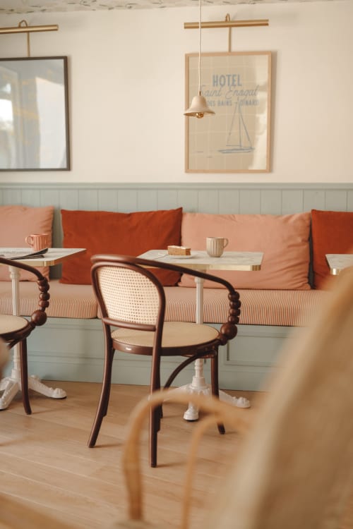 Espace café de l'Hôtel Saint Enogat avec banquette rouge capitonnée, fauteuils en rotin et décor nautique à Dinard