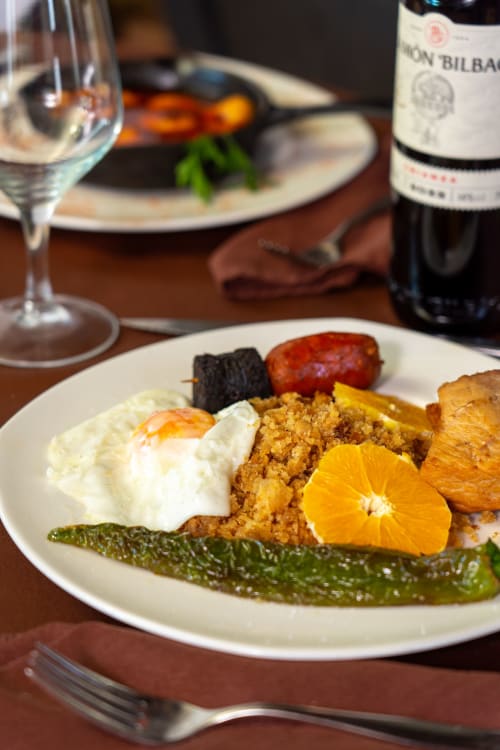 Gourmet-Gericht des Hotel Balcón De Los Montés mit pochiertem Ei, Gemüse und Orangengarnitur, serviert mit Wein