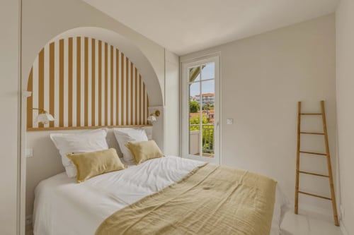 Chambre moderne aux Suites Du Port à Arcachon avec tête de lit cintrée, touches dorées et balcon vue mer