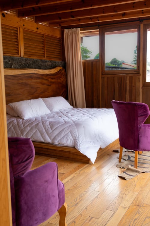 Wooden canopy bed with white bedding and purple velvet chairs in La Hacienda Tepoztlán bedroom