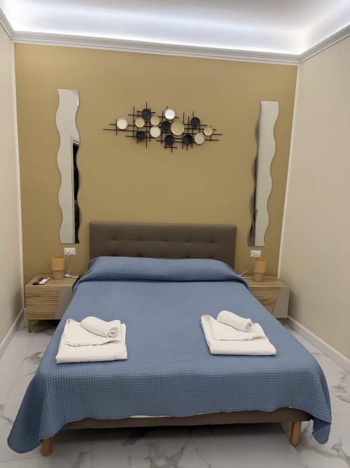 Camera da letto moderna allo Zappy Domus B&B di Taranto con biancheria blu, parete accent dorata e arte contemporanea