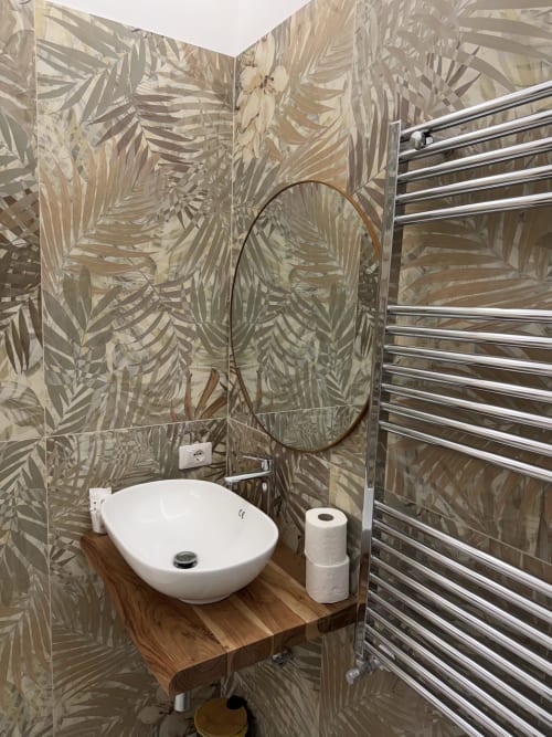 Bagno moderno dello Zappy Domus B&B a Taranto con carta da parati a foglie tropicali, lavabo bianco su ripiano in legno e scaldasalviette