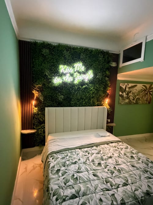 Camera da letto moderna con parete accent verde, insegna neon, rigoglioso sfondo botanico e biancheria a tema vegetale presso Zappy Domus a Taranto
