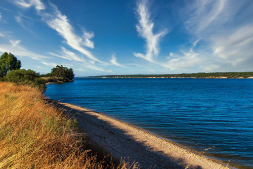 Lago azul pristino com praia de relva dourada e costa florestada em Monte da Tojeirinha, Montargil Portugal