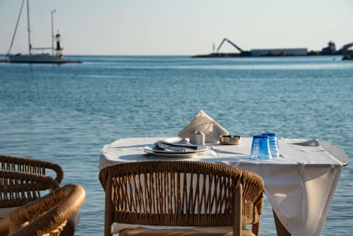 Waterfront dining at Villa Annette with rope chairs, white table, and sailboats anchored in blue Mediterranean waters