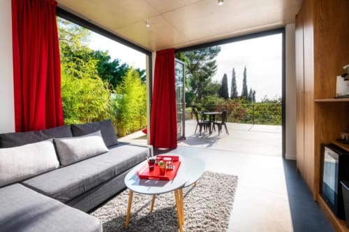 Modern living room at Villa Annette with gray sofa, red curtains, and terrace overlooking gardens in France