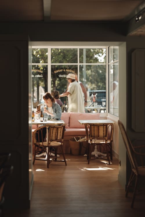 Terrasse ensoleillée de la cafétéria de l'Hôtel Saint Enogat à Dinard avec chaises vintage et grandes fenêtres donnant sur la rue