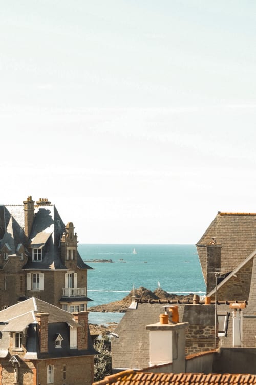 Vue côtière de l'Hôtel Saint Enogat à Dinard avec mer turquoise et voiliers visibles entre les bâtiments en pierre