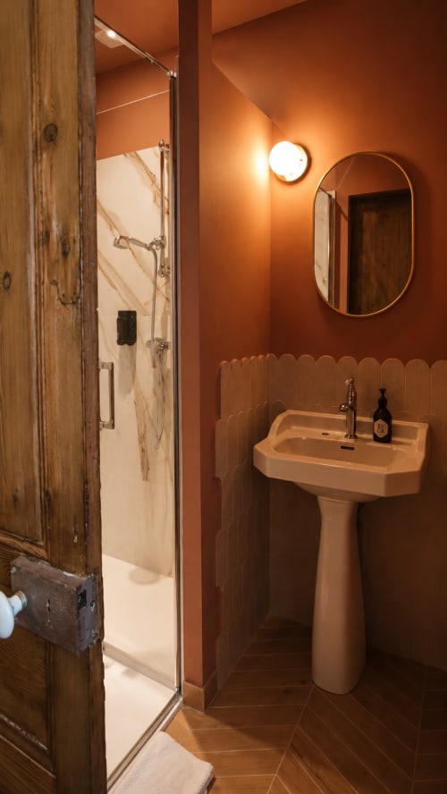 Stylish bathroom at La Maison 1903 with terracotta walls, pedestal sink, and walk-in shower
