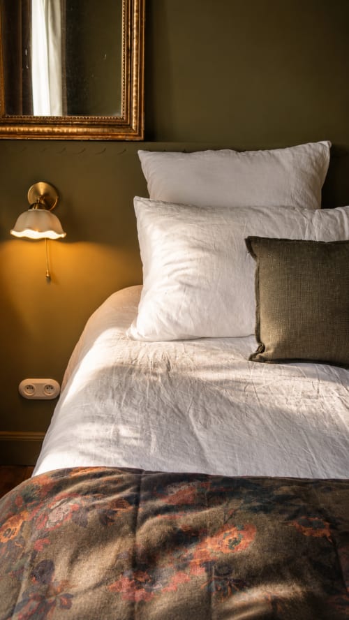 Elegant bedroom at La Maison 1903 B&B with olive walls, white linens, gold-framed mirror, and brass sconce lamp