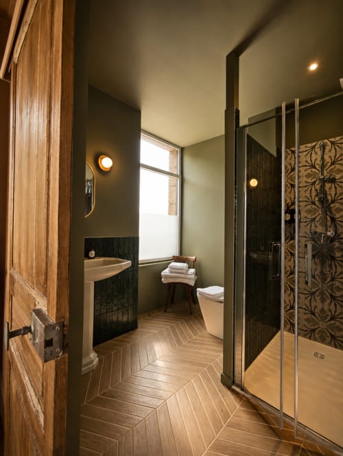 Modern bathroom at La Maison 1903 B&B in Trévou-Tréguignec with dark walls, herringbone flooring, pedestal sink, and glass