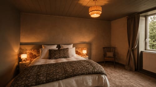 Warm, elegantly lit master bedroom at La Maison 1903 B&B in Trévou-Tréguignec with patterned bedding and ambient ceiling