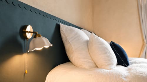 Elegant bedroom at La Maison 1903 B&B with white pillows, brass wall sconce, and dark accent wall in Trévou-Tréguignec.