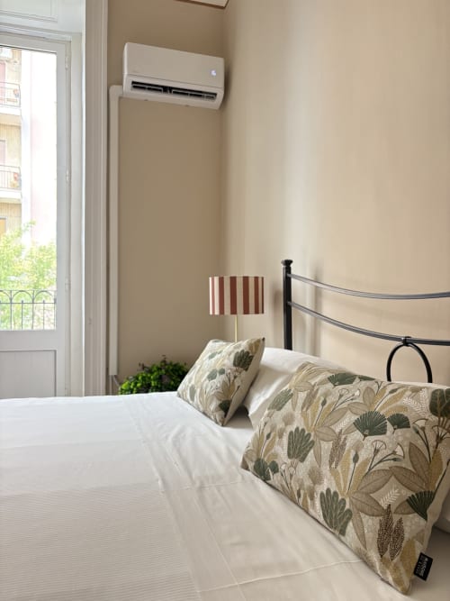 Camera da letto moderna con biancheria bianca, cuscini decorativi, letto in metallo, climatizzatore a parete e balcone con vista sulla città