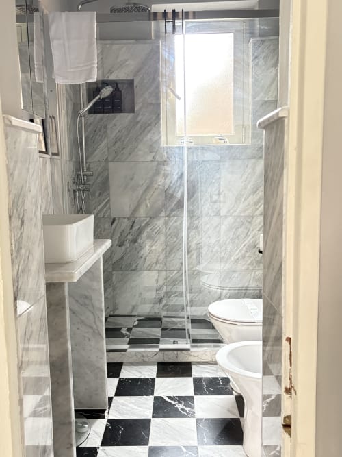 Bagno moderno con piastrelle in marmo, pavimento a scacchiera, cabina doccia in vetro e bidet a Sicily In Home Catania