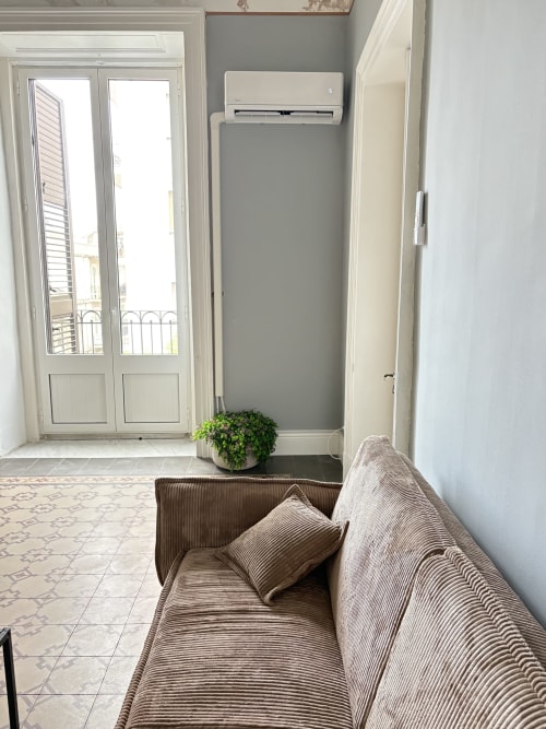 Moderna camera a Catania con divano beige, aria condizionata, porte-finestre al balcone e piante verdi