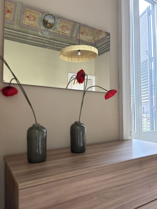 Camera moderna presso Sicily In Home Catania con arredamento minimalista: due vasi neri con fiori rossi, scrivania in legno e elementi decorativi