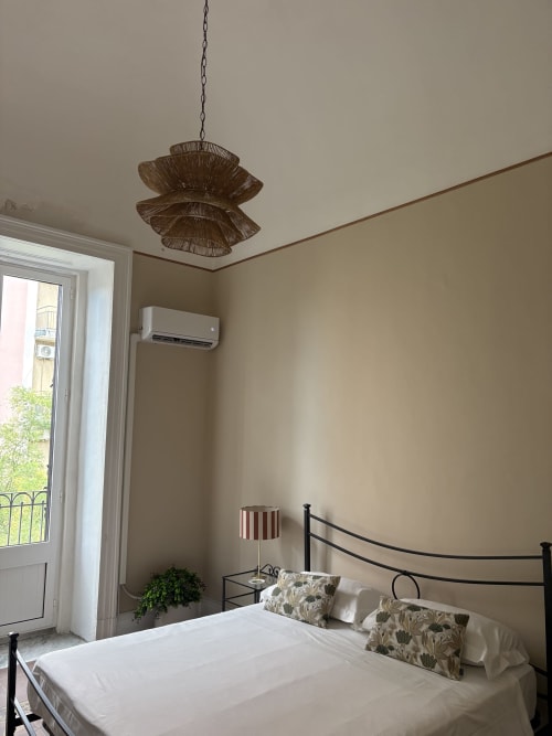 Camera luminosa In Home hotel a Sicilia con letto in ferro battuto, lampada a sospensione intrecciata, aria condizionata e vista su Catania