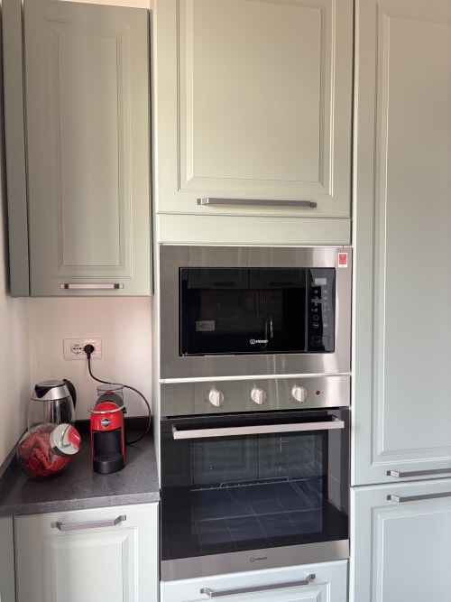 Angolo cucina moderno con cabinetry bianca, microonde e forno Indesit in acciaio inox, caffettiera rossa e piano di lavoro scuro