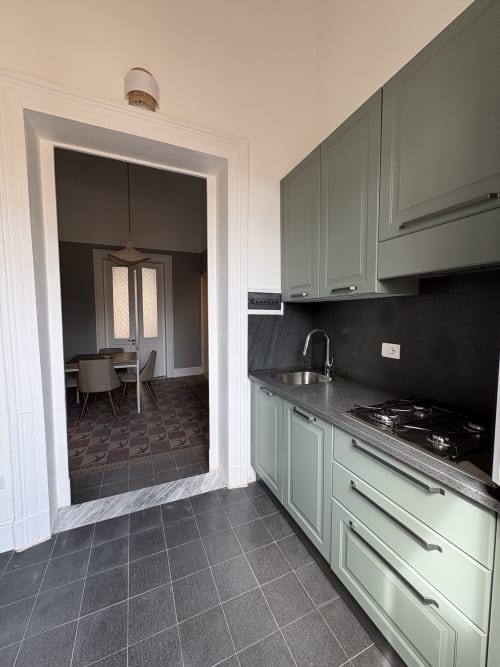 Cucina moderna con ante verde salvia, piano in granito nero, fornello a gas e accesso alla sala da pranzo nell'appartamento di Catania