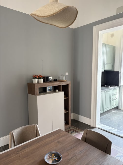 Elegante zona pranzo dell'appartamento In Home Catania a Sicilia con tavolo in legno, pareti grigie e cucina contemporanea