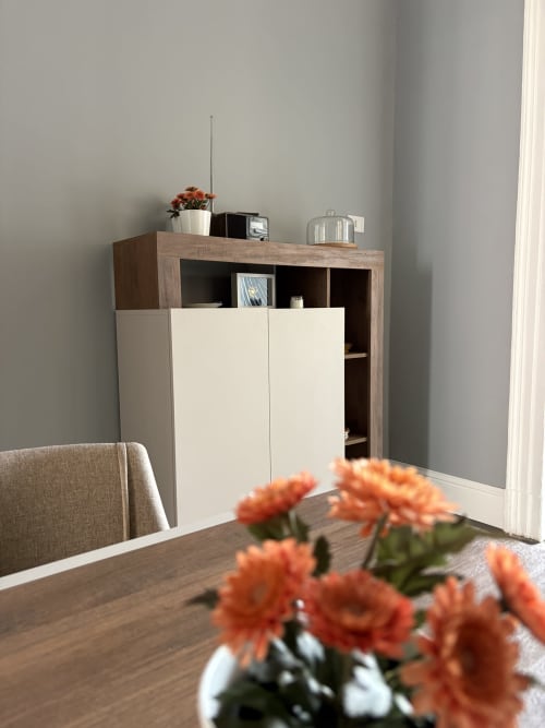 Sala da pranzo moderna a Sicily In Home con tavolo in legno, fiori arancioni, sedia beige e mobile contenitore