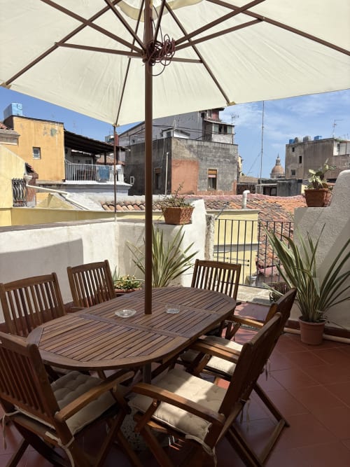 Terrazza panoramica con area ristorazione a Catania, Sicilia: arredamento in legno e ombrellone con vista sui palazzi storici