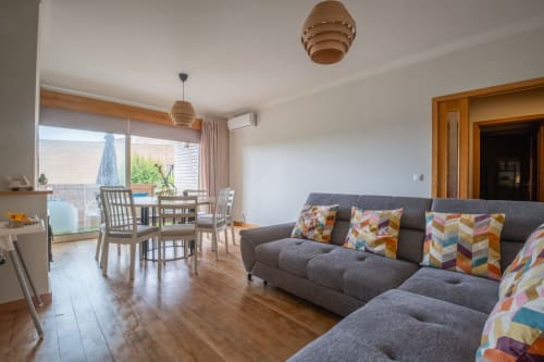Modernes Wohnzimmer mit grauem Sofa, farbigen Kissen, Essbereich und Stadtblick in der FamilyHub EcoHost Wohnung in Porto