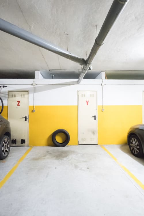 Unterirdische Parkgarage des EcoHost Porto mit gelb markierten Parkplätzen, nummerierten Lagereinheiten Z und Y und einem angelehnten Reifen
