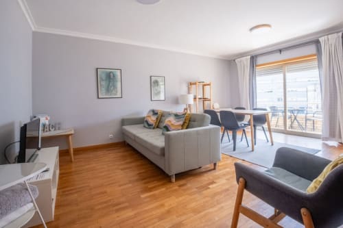 Modernes Wohnzimmer in der OceanSide-Wohnung in Matosinhos mit grauem Sofa, Holzböden und Stadtblick von den Balkontüren.