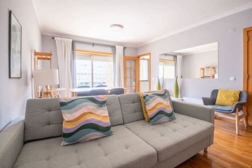 Modernes Wohnzimmer mit grauem Sofa, bunten Kissen, Holzmöbeln und Stadtblick im EcoHost Apartment in Matosinhos