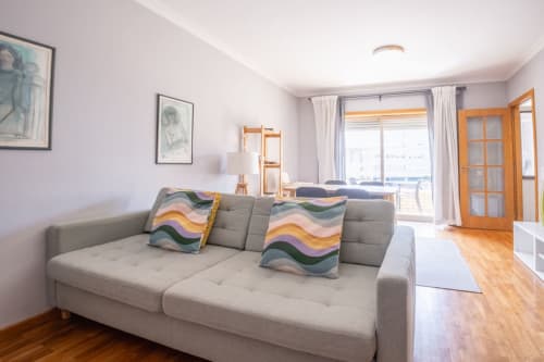 Modernes Wohnzimmer mit grauem Sofa, bunten Kissen, Holztüren und Stadtblick im OceanSide Apartment in Matosinhos