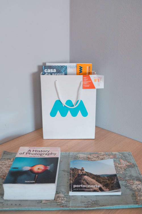 Weiße Einkaufstasche mit türkisem Wellen-Logo mit Magazinen im EcoHost Matosinhos Apartment, mit ausgestellten Reisebüchern