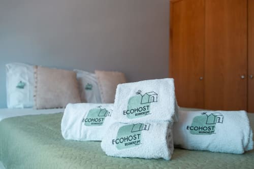 Aufgerollte weiße Handtücher mit EcoHost-Branding auf einem grünen Bett im Apartment OceanSide, Matosinhos