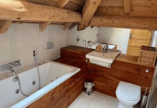 Salle de bain luxueuse avec poutres en bois, baignoire, toilettes et double lavabo aux Chalets d'Aline à La Plagne