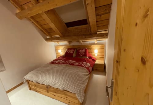 Chambre cosy avec poutres apparentes, literie rouge et mobilier intégré en bois aux Chalets d'Aline, La Plagne.