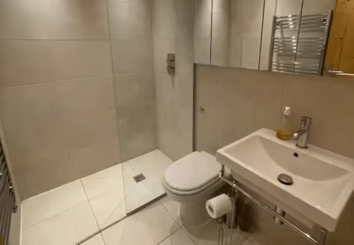 Salle de bains moderne aux Chalets d'Aline à La Plagne : carrelage blanc, toilettes, lavabo et douche vitrée.