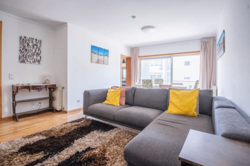 Modernes Wohnzimmer mit grauem Ecksofa, gelben Kissen, Holzböden und Balkon mit Stadtblick im EcoHost Arcozelo