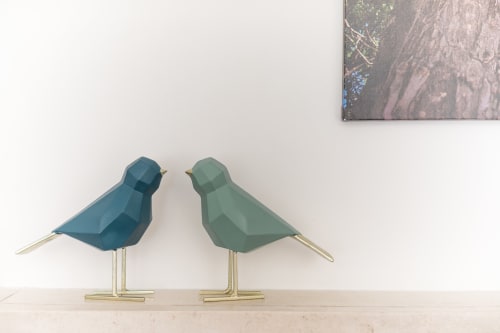 Zwei geometrische Vogelskulpturen in Blau und Grün mit Messingbeinen auf einem Regal in der EcoHost-Wohnung in Arcozelo